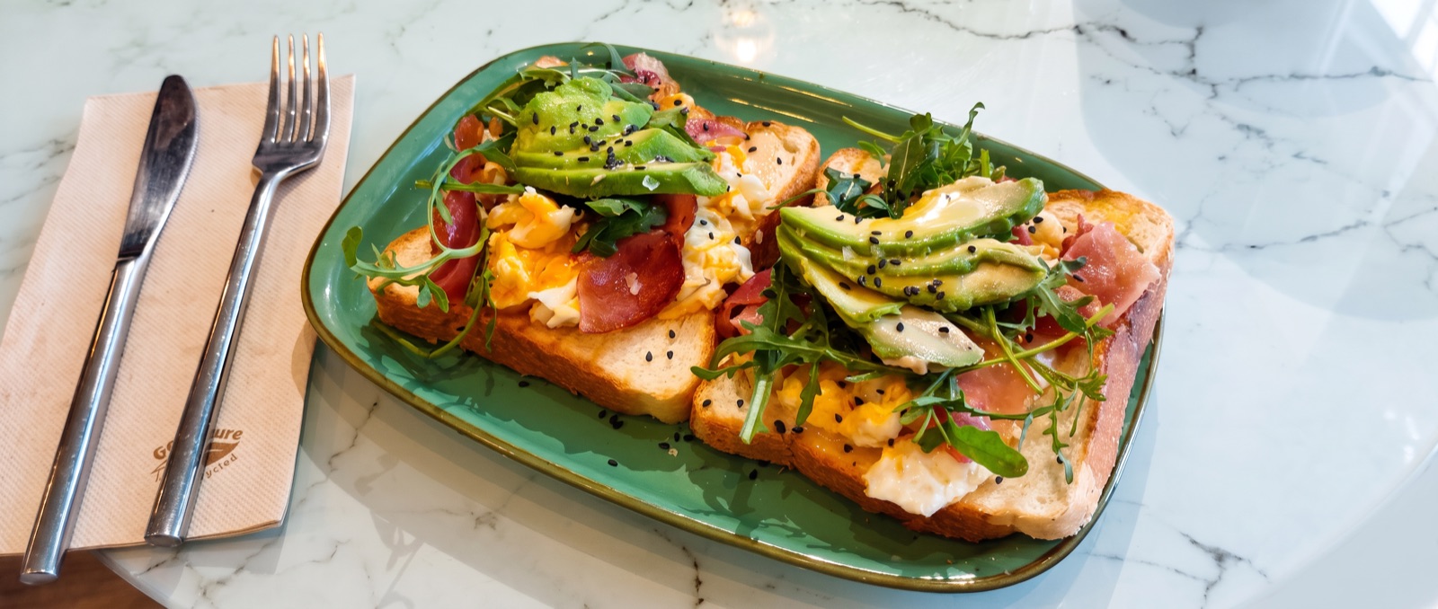 Tosta con aguacate, jamón y huevo en plato verde