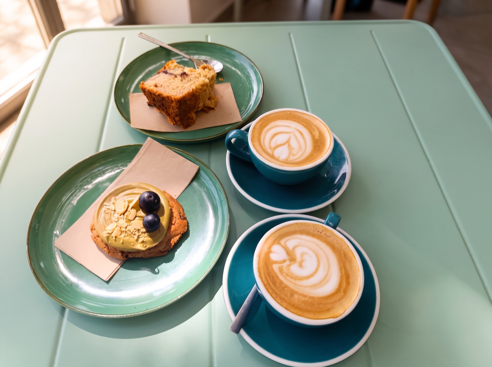 Dos cafés con latte art y una tarta sobre la mesa verde agua